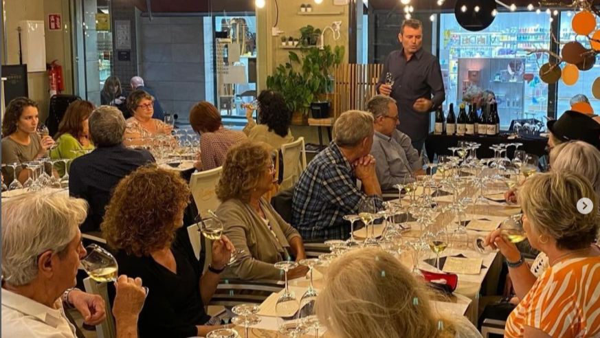 Diners seated at a wine dinner listen to the speaker, who is standing.