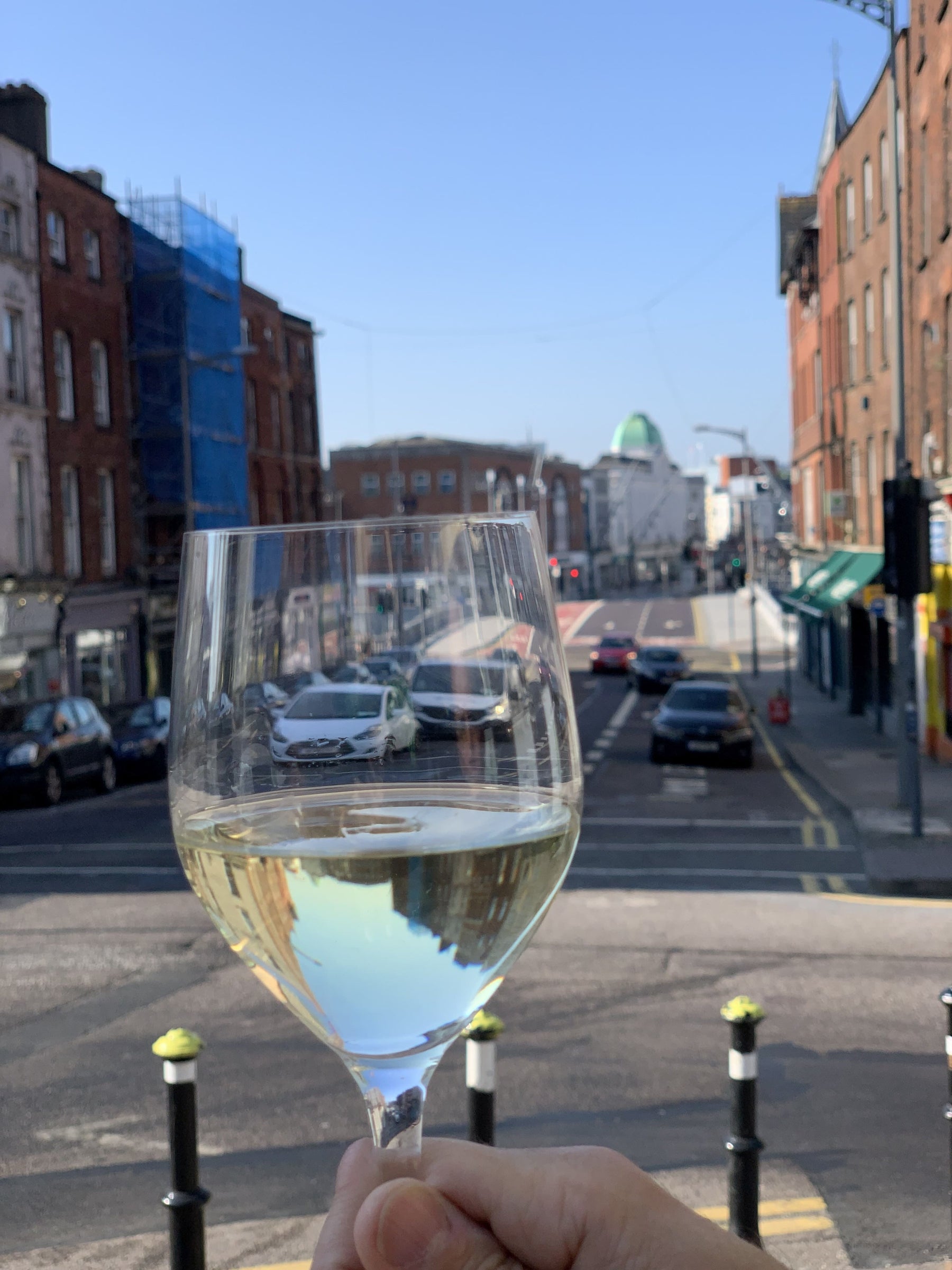 Glass of white wine being held with a view of Patrick Street, Cork in the background.